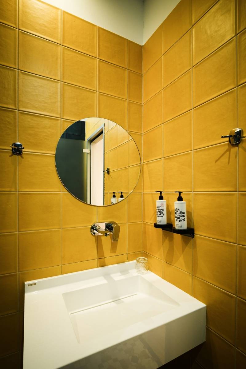 Dettaglio bagno con piastrelle senape e specchio rotondo