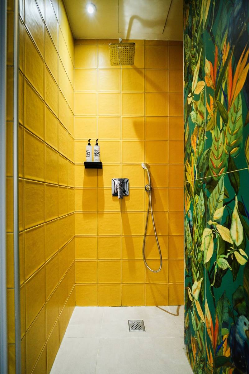 Dettaglio doccia con piastrelle senape e vetro con murale jungle